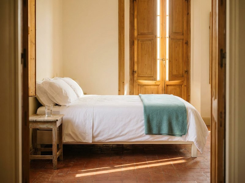 cheapest countries to travel — a simple guesthouse room with white linens and shuttered windows, herowncompass.com